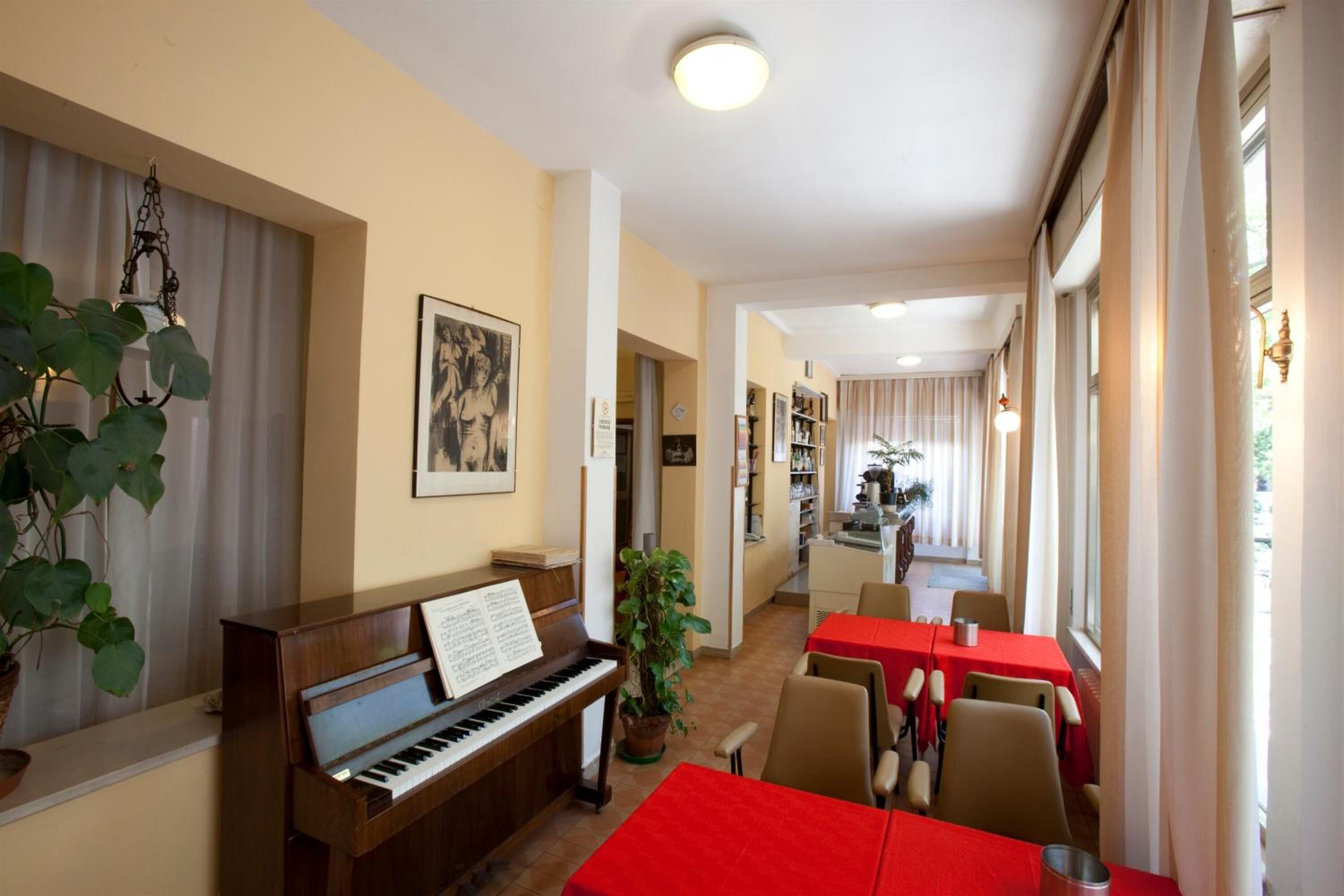 Un comedor con un piano, mesas y sillas rojas.