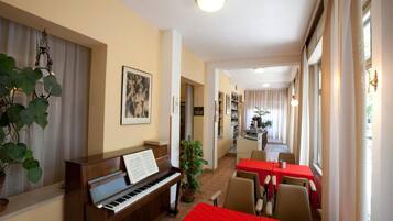 Un comedor con un piano, mesas y sillas rojas.