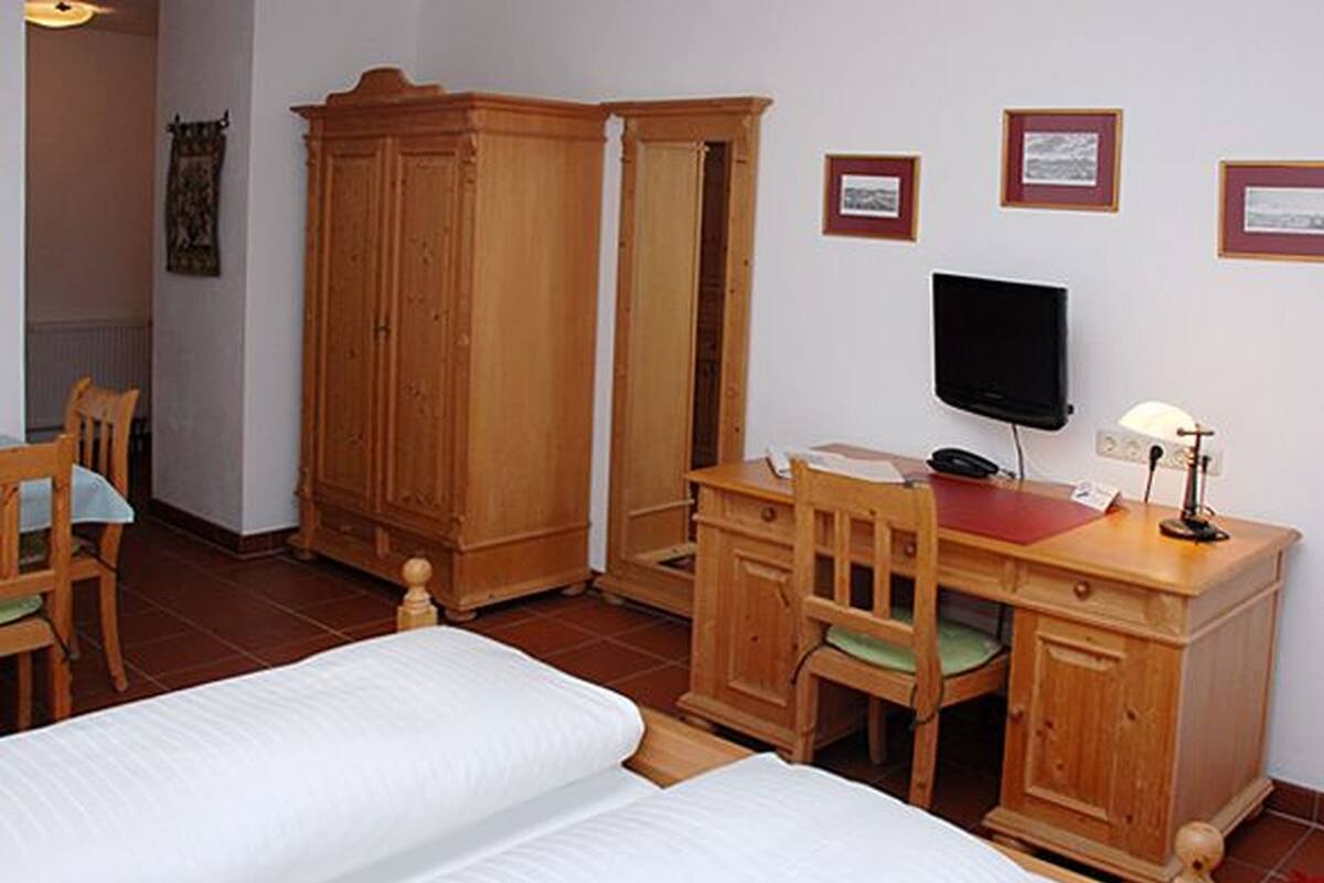 A room with two beds, a wooden desk with a chair, a television, and a wardrobe.