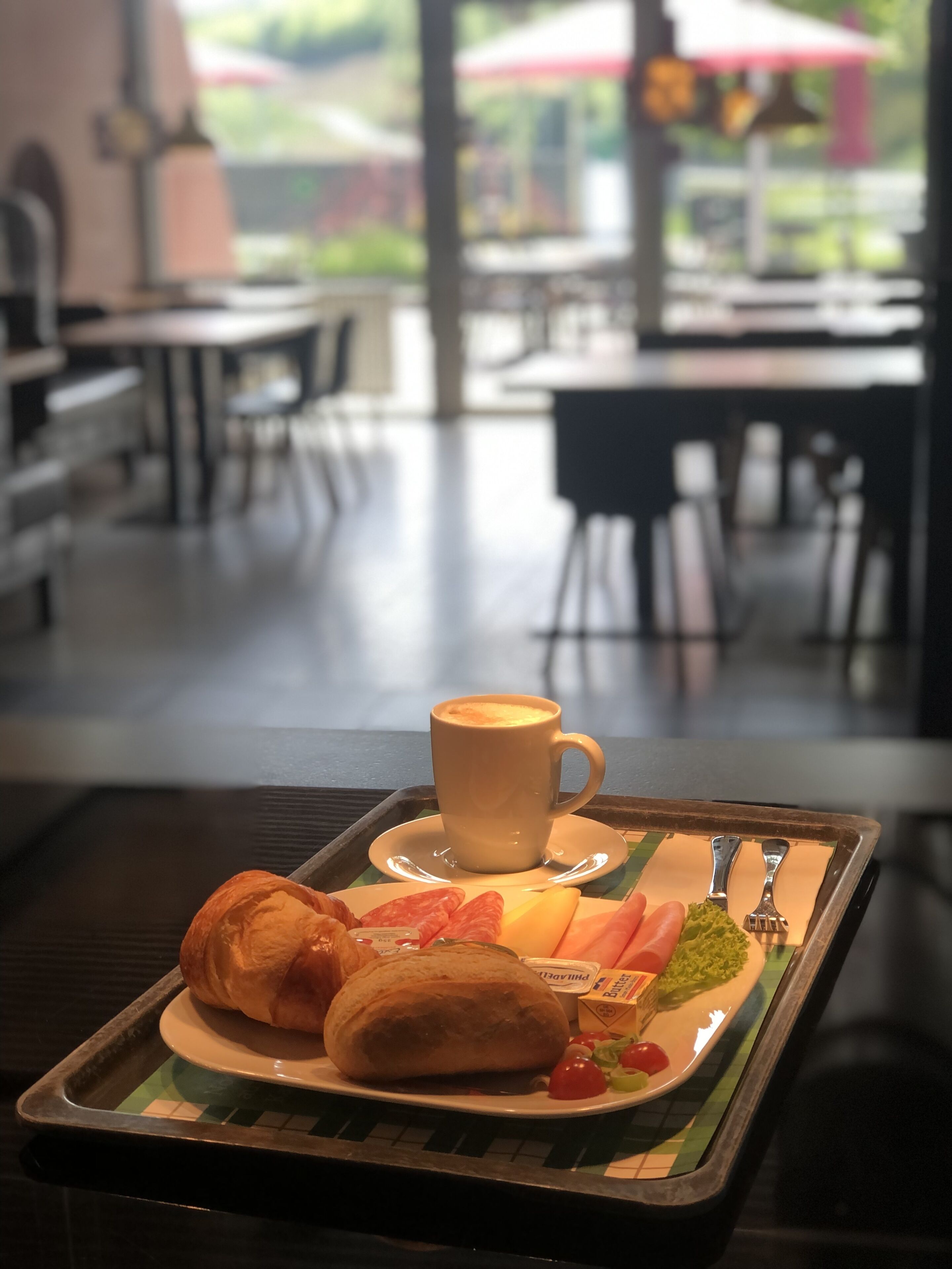 Una bandeja con un croissant, un pastel, una taza de café y un plato con tomates y verduras.