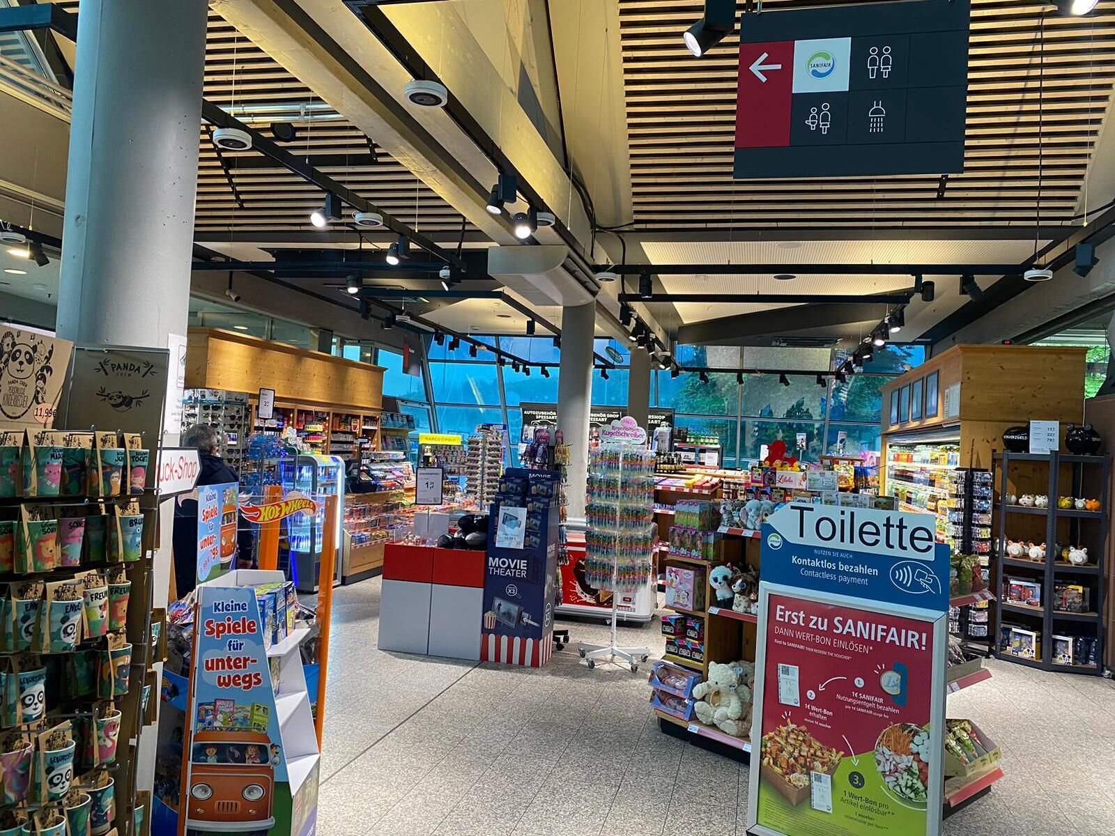 Een supermarkt interieur met verschillende productstellingen, een bioscoopgedeelte en een bord dat de locatie van het toilet aangeeft.