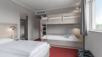 A hotel room with two beds, a wardrobe, a mirror, a bedside table, and a window.