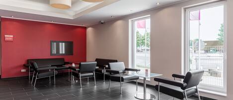A modern waiting area with a red wall, black and white chairs, and a large window with a view of the outside.