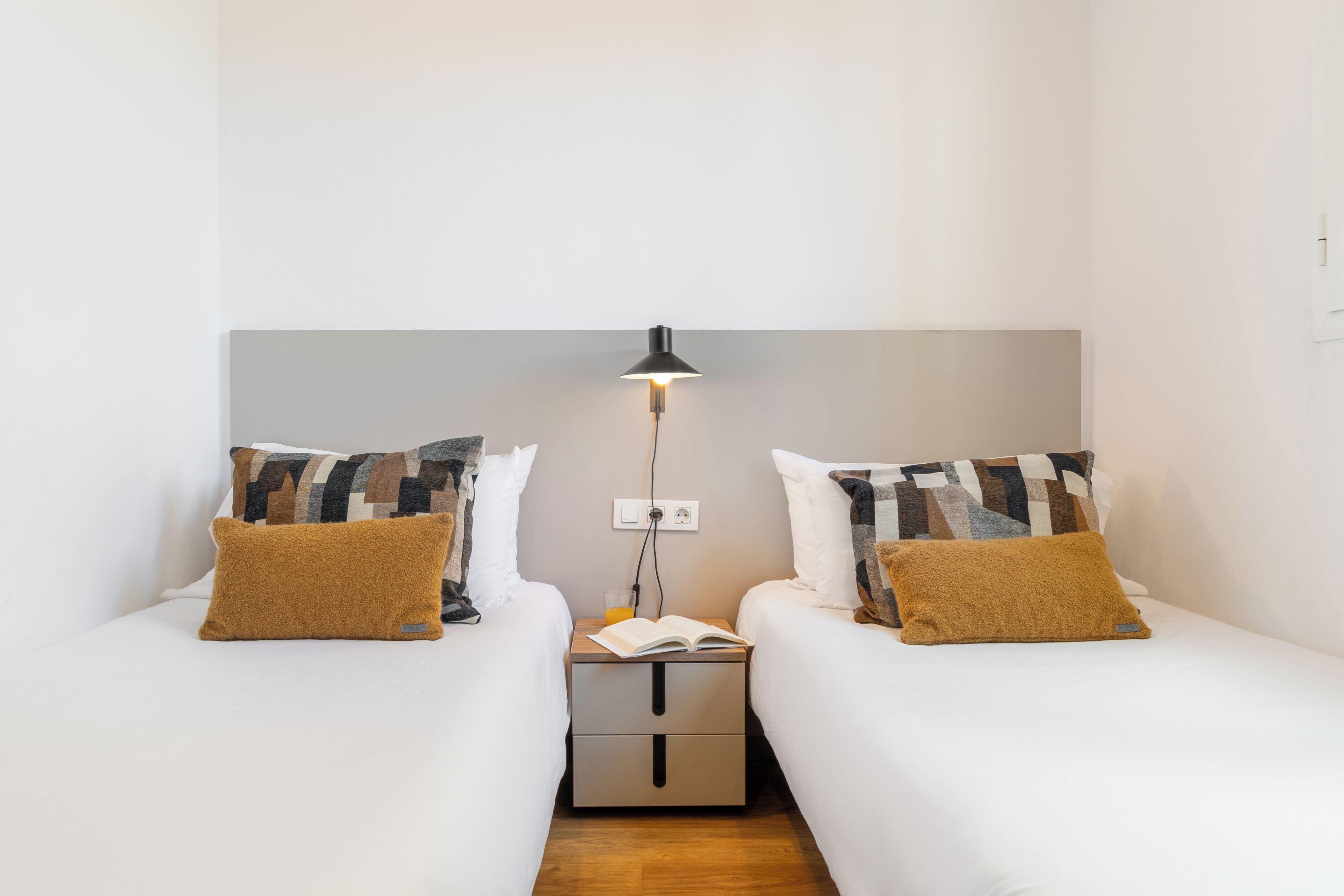 A twin bedroom with two beds, a nightstand with a lamp, and a book.