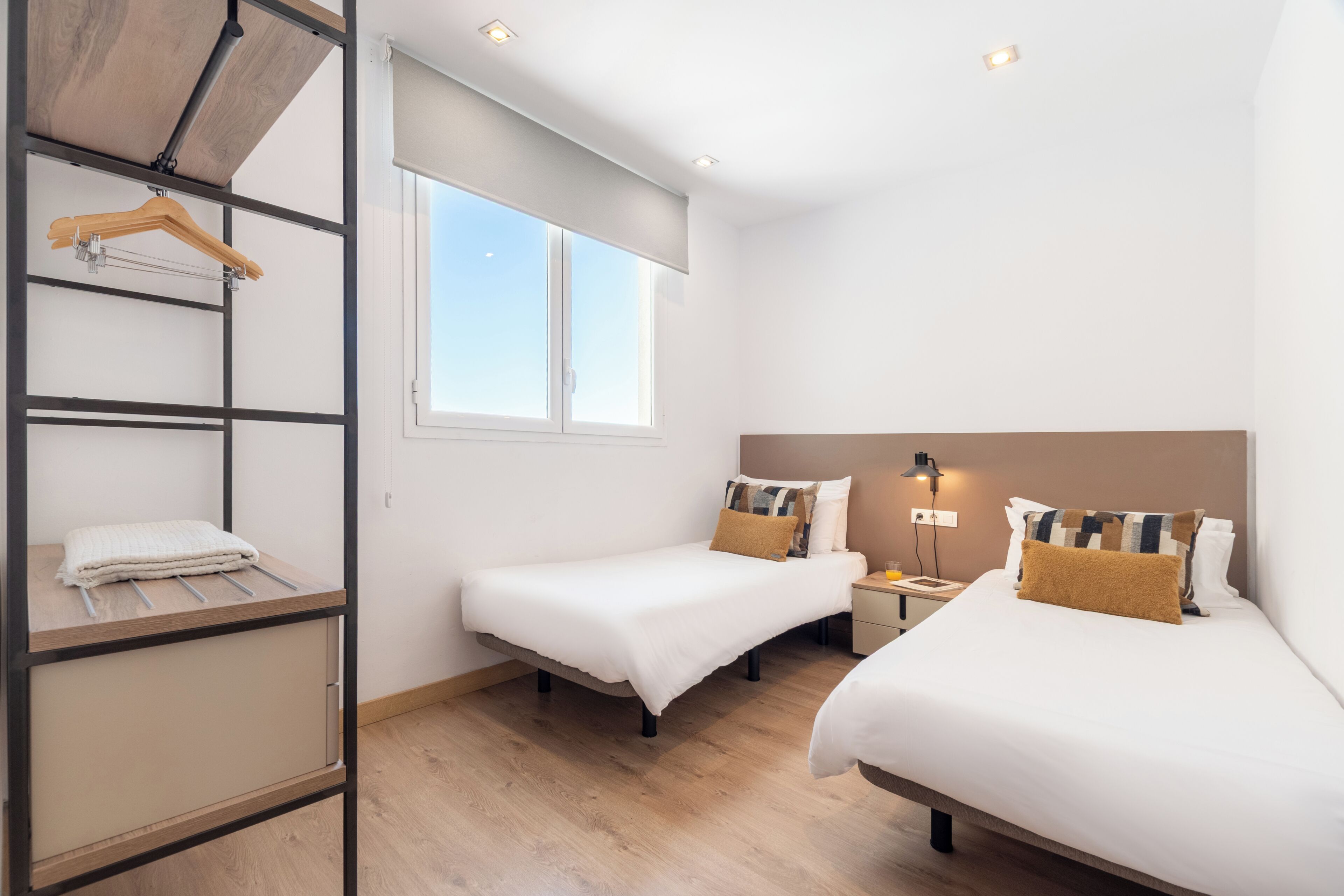 Una habitación de hotel con dos camas, un armario, una ventana y una mesita de noche con lámpara.