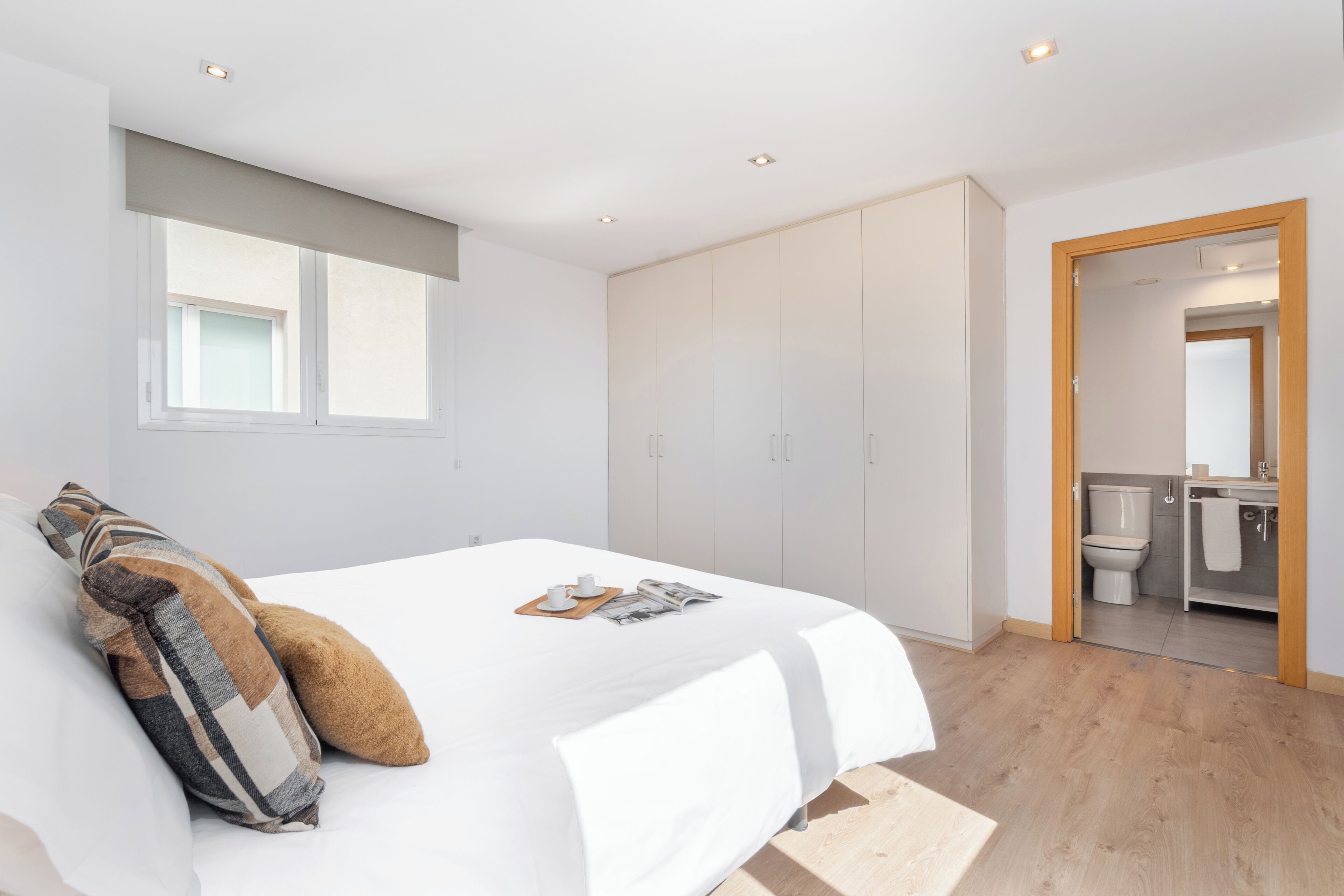 Een moderne slaapkamer met een groot bed, een kledingkast en een badkamer zichtbaar door een open deur.