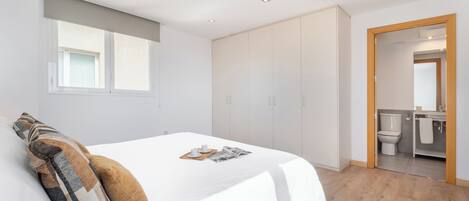 Een moderne slaapkamer met een groot bed, een kledingkast en een badkamer zichtbaar door een open deur.