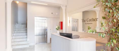 A reception area with a modern design, featuring a reception desk, a staircase, and a large mirror reflecting the interior.