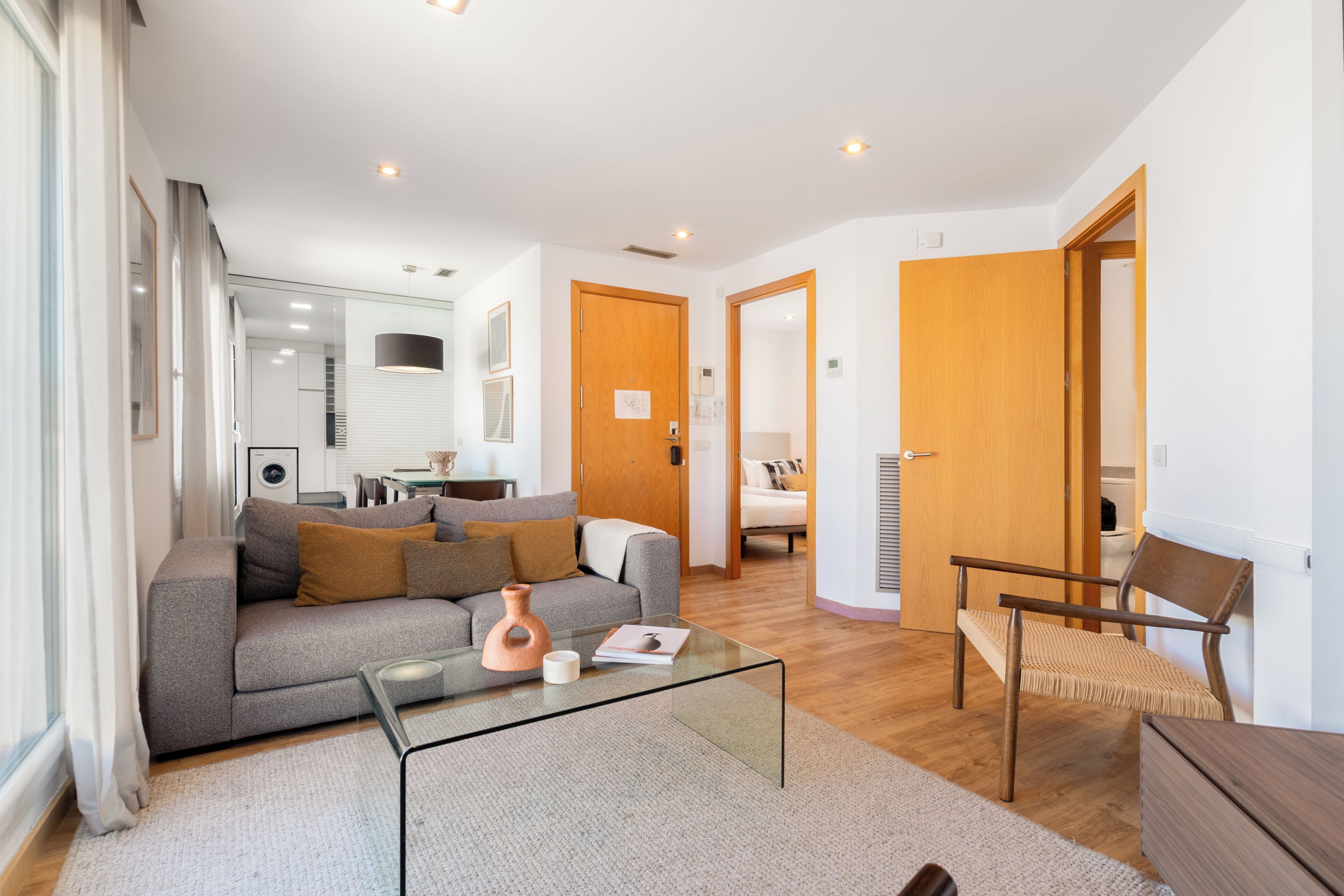 A modern living room with a sofa, coffee table, and a chair. There is a wooden door and a white wall.