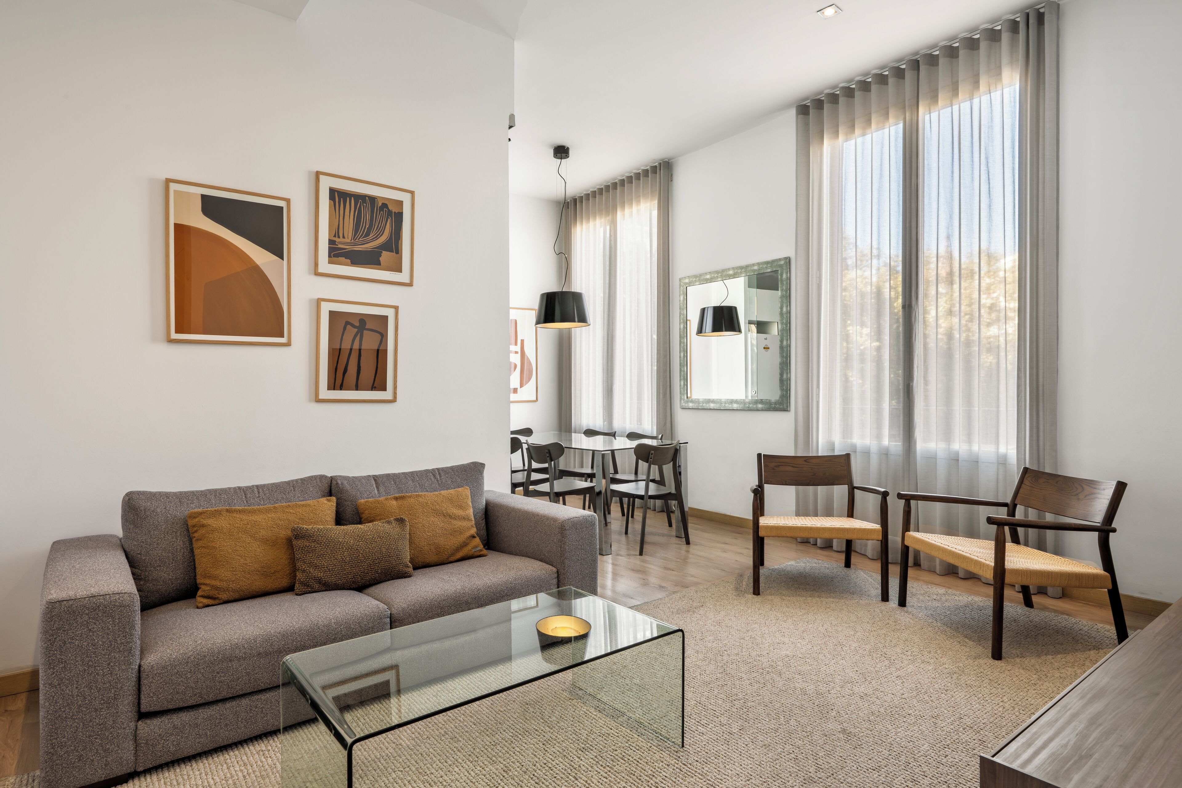 Een moderne woonkamer met een grijze bank, een glazen salontafel en een eethoek met een tafel en stoelen.