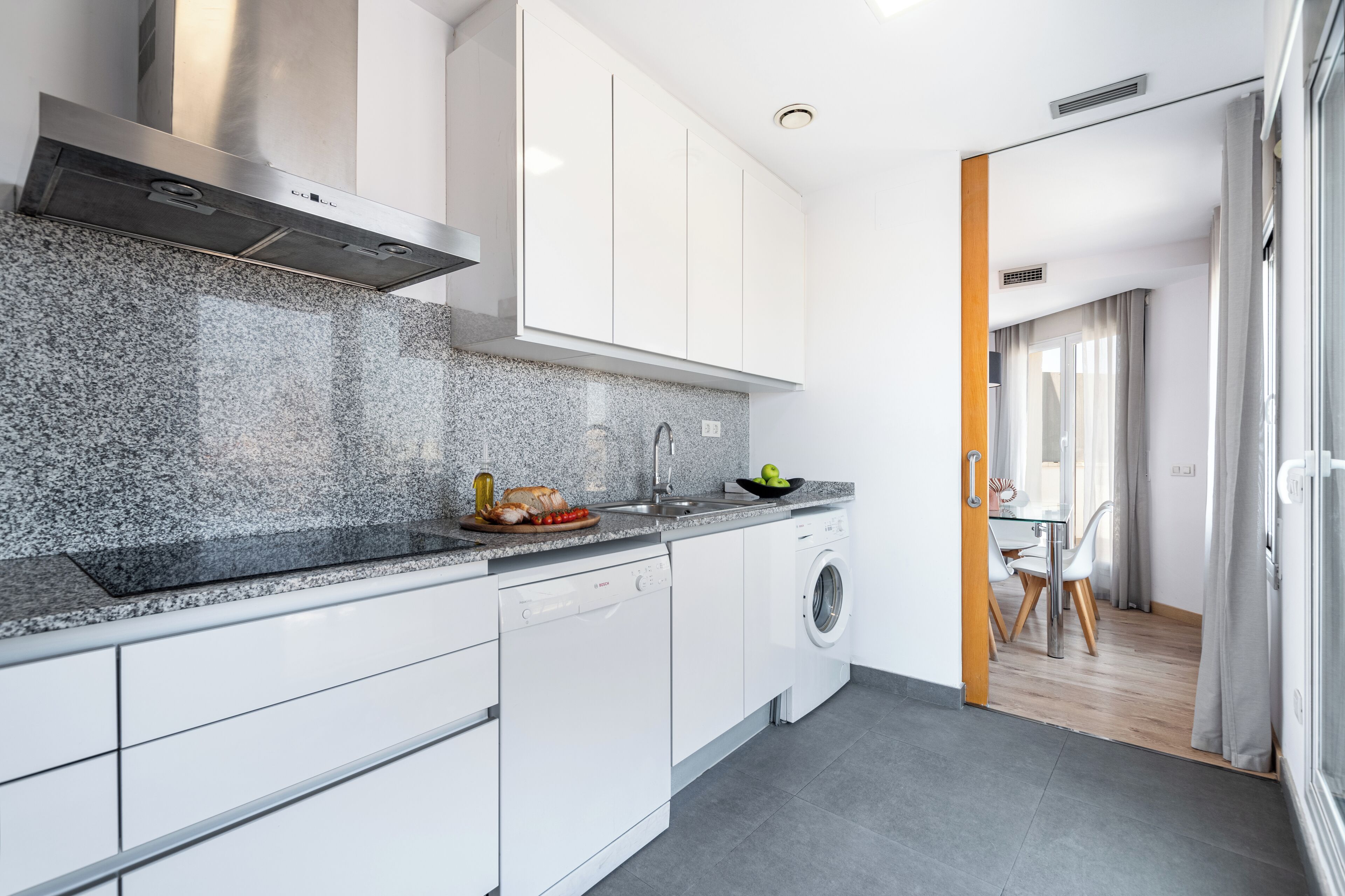 A modern kitchen with white cabinets, a granite countertop, a dishwasher, and a washing machine.