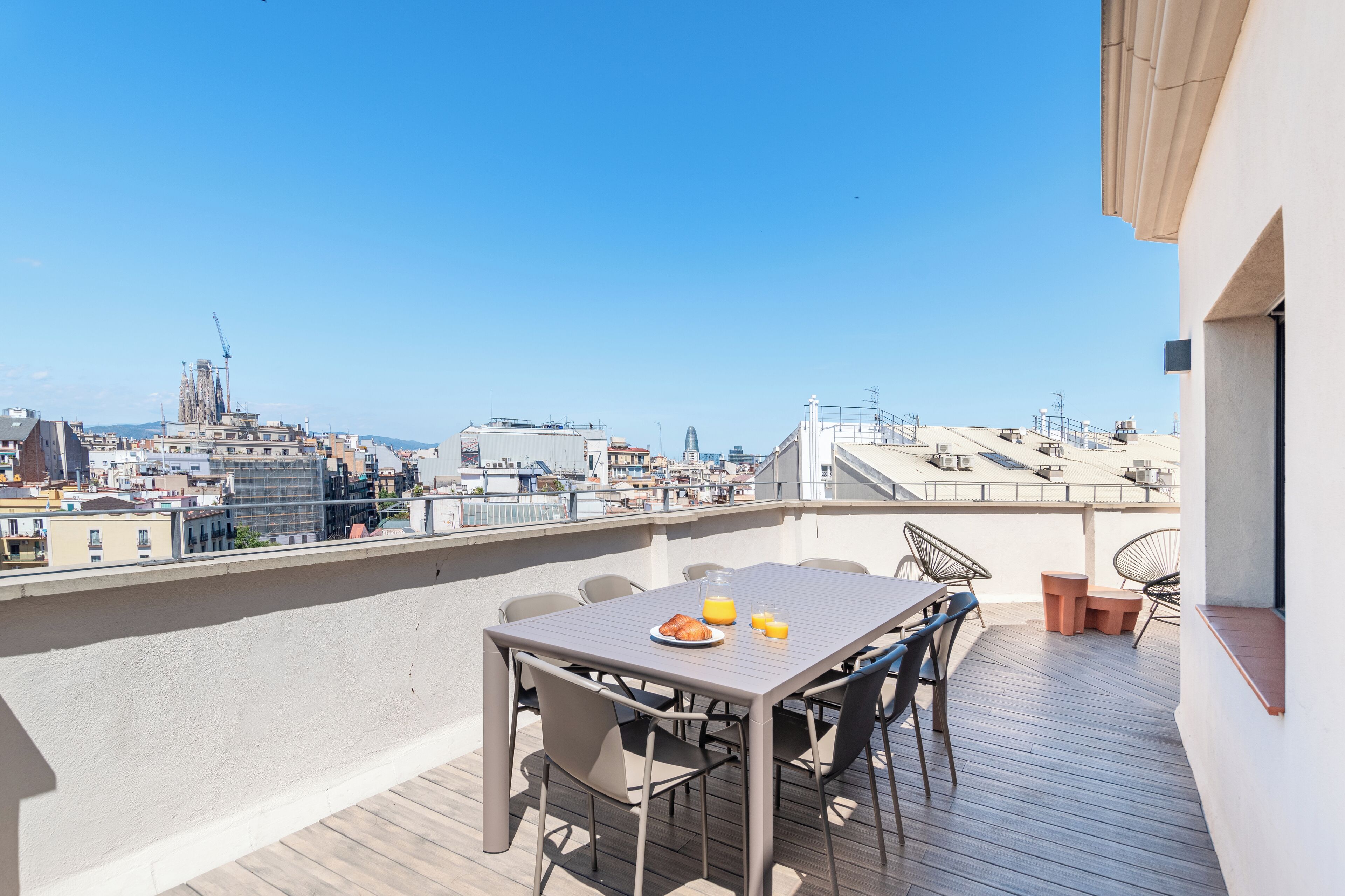 Una terraza en la azotea con una mesa preparada para dos personas, vistas a la ciudad y una grúa al fondo.