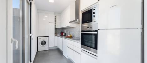 Una cocina moderna con armarios blancos, un horno Bosch, lavavajillas y lavadora.