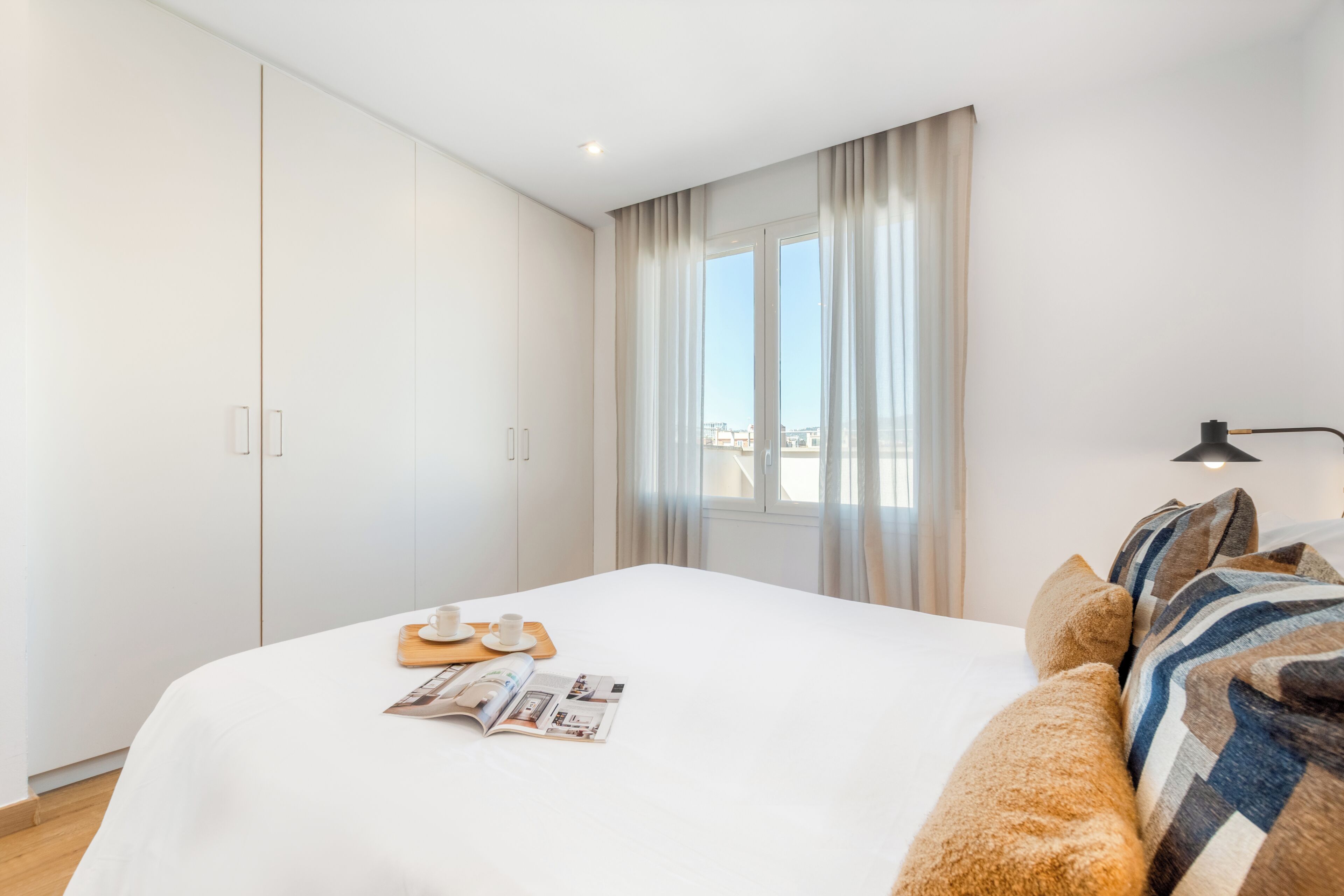 A neatly arranged bedroom with a bed, a window with curtains, and a bedside table with a lamp.