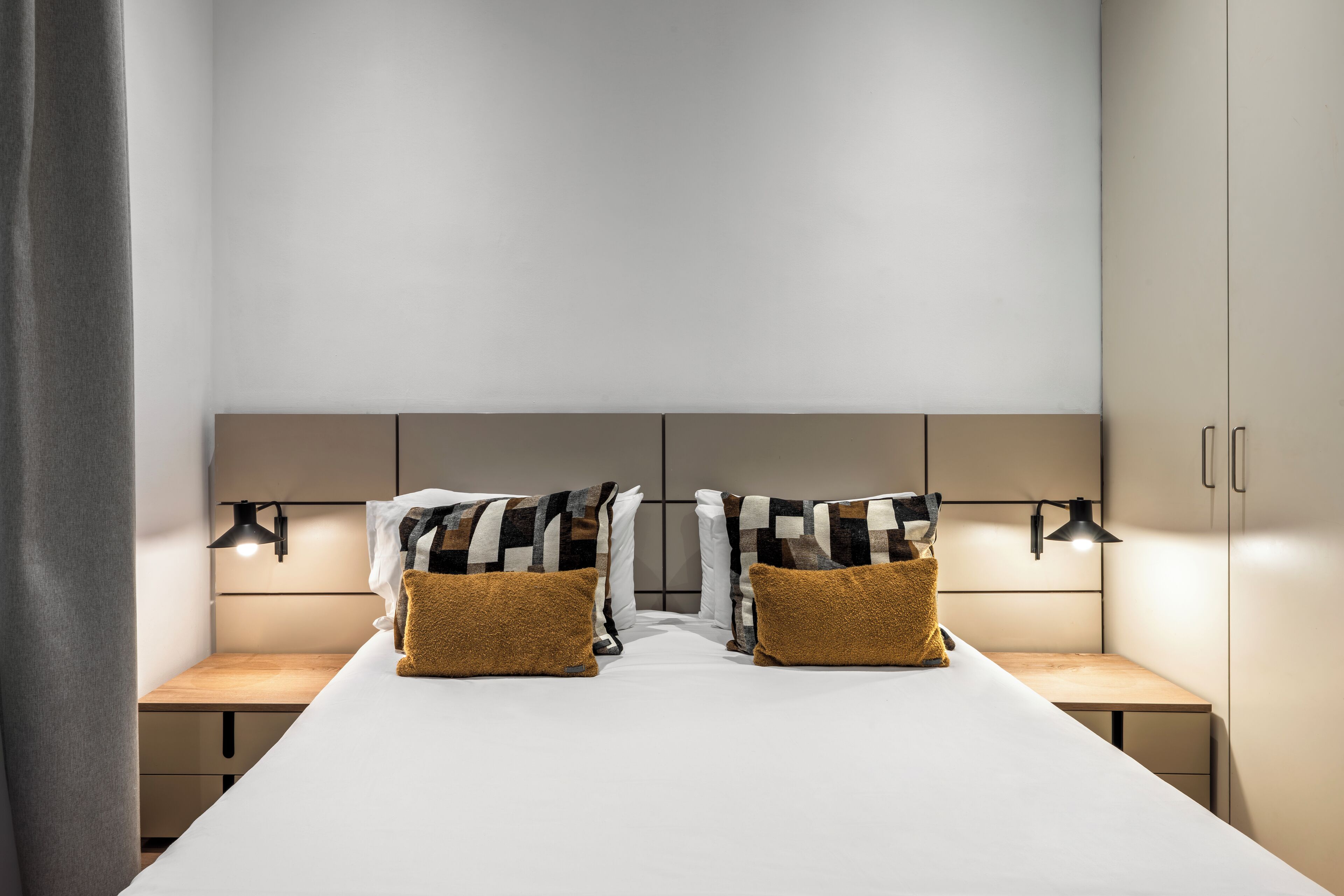 Ein modernes Hotelzimmer mit einem großen Bett, zwei Nachttischen und einem Kopfteil mit integrierter Beleuchtung.