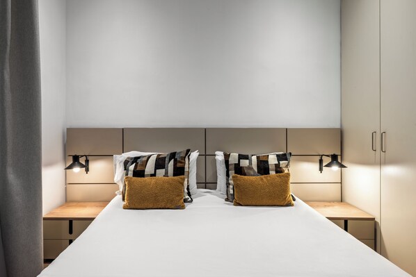 Una habitación de hotel moderna con una cama grande, dos mesitas de noche y un cabecero con iluminación integrada.