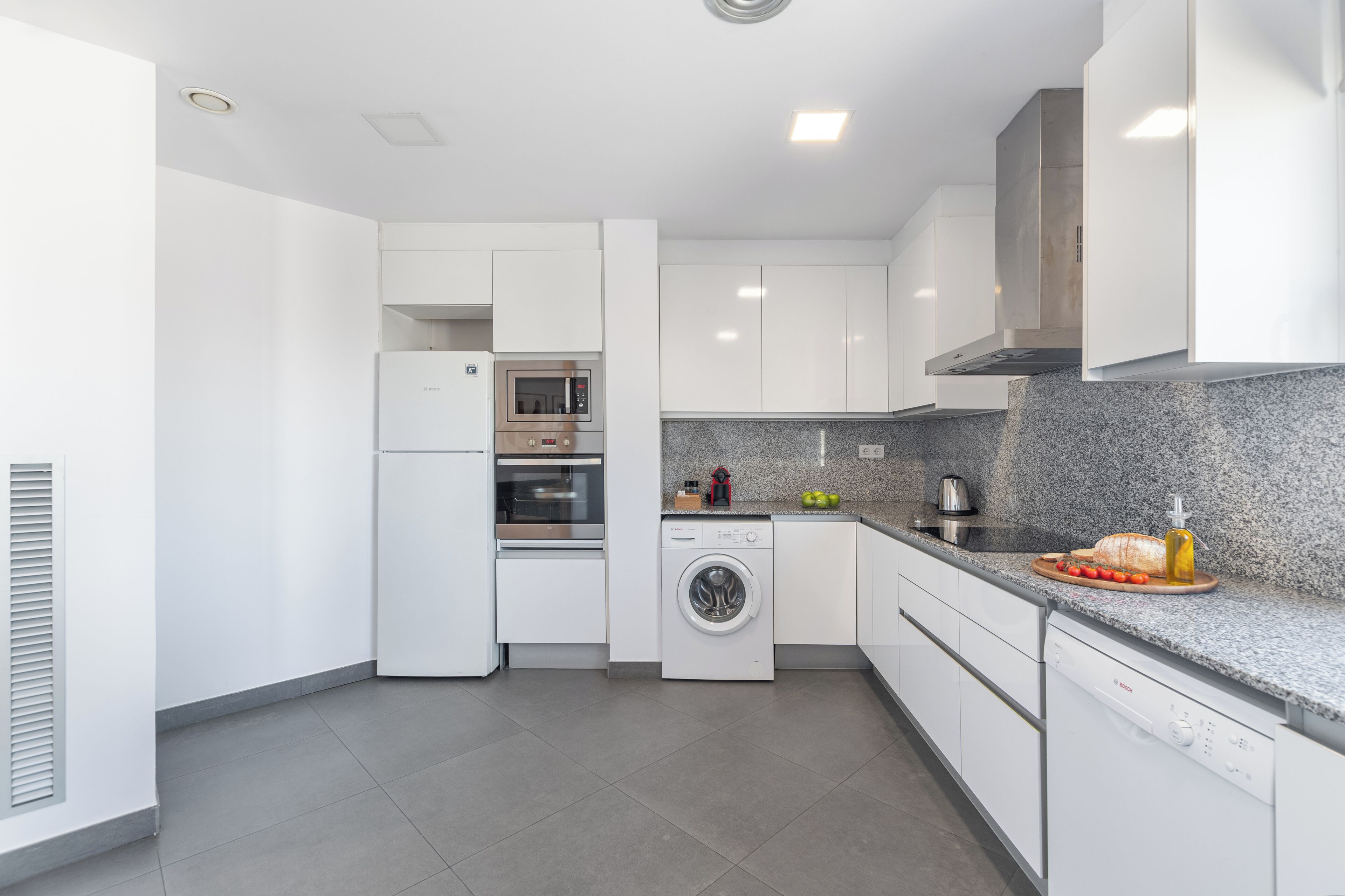 A modern kitchen with white cabinets, a built-in oven, microwave, and dishwasher.