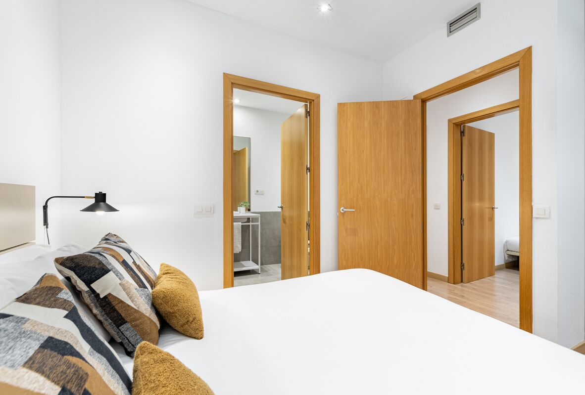 A modern bedroom with a large bed, a bedside lamp, and wooden doors leading to other rooms.