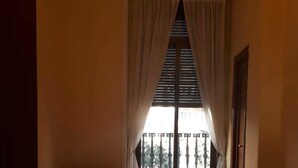 A room with two beds, a wooden table, and a window with a view of a balcony. - Hostal Pacios (Madrid)