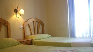 A hotel room with two single beds, a nightstand, a wall-mounted lamp, and a window with curtains. - Hostal Pacios (Madrid)