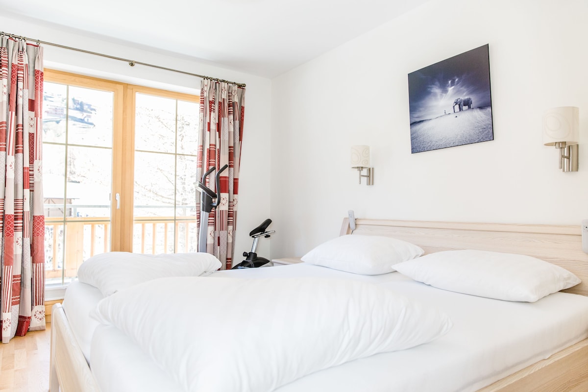 A hotel room with a large bed, a bicycle, and a view of the outdoors through a window.