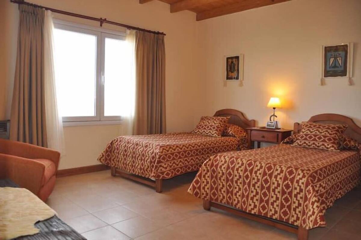 A bedroom with two beds, a nightstand, a lamp, and a window with curtains.