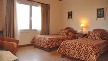 A bedroom with two beds, a nightstand, a lamp, and a window with curtains.