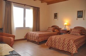 Un dormitorio con dos camas, una mesita de noche, una lámpara y una ventana con cortinas.