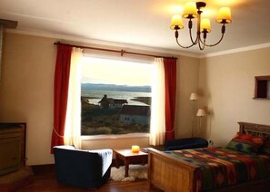 Una habitación con cama, una silla, una mesita y una ventana con cortinas.
