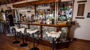 Una zona de bar con taburetes, una pared de piedra y una variedad de botellas y vasos.