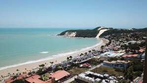 A coastal town with a beach, residential buildings, and a hilly backdrop. - Kuara Hostel Natal (Parnamirim)