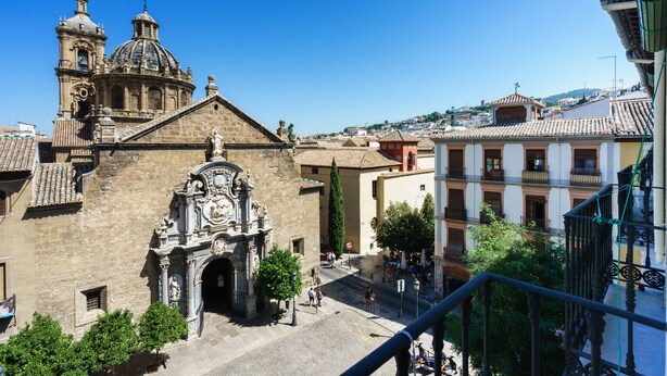 Un edificio histórico con una cúpula destacada y un campanario, un arco central y una calle con peatones.