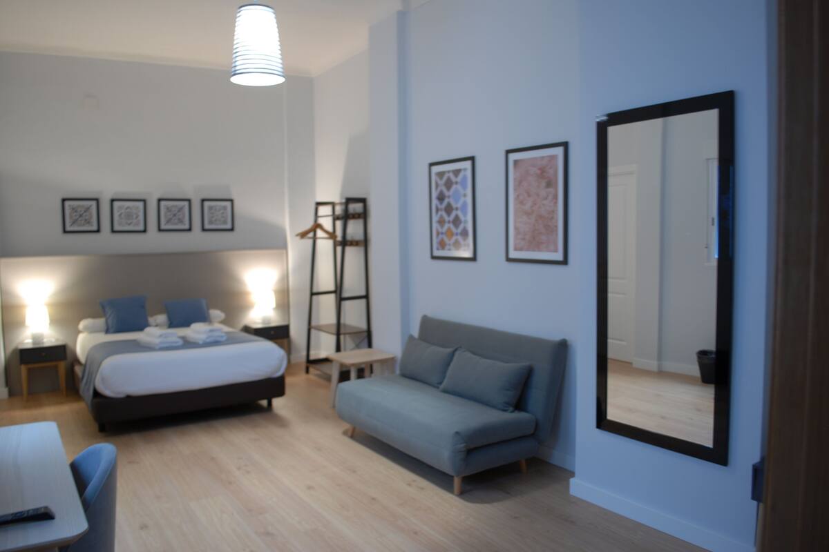 Quarto moderno com cama, sofá, escrivaninha e um espelho grande.