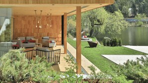 A modern outdoor seating area with wooden flooring, a glass wall, and a view of a lake. - Hotel Weihrerhof (Renon)