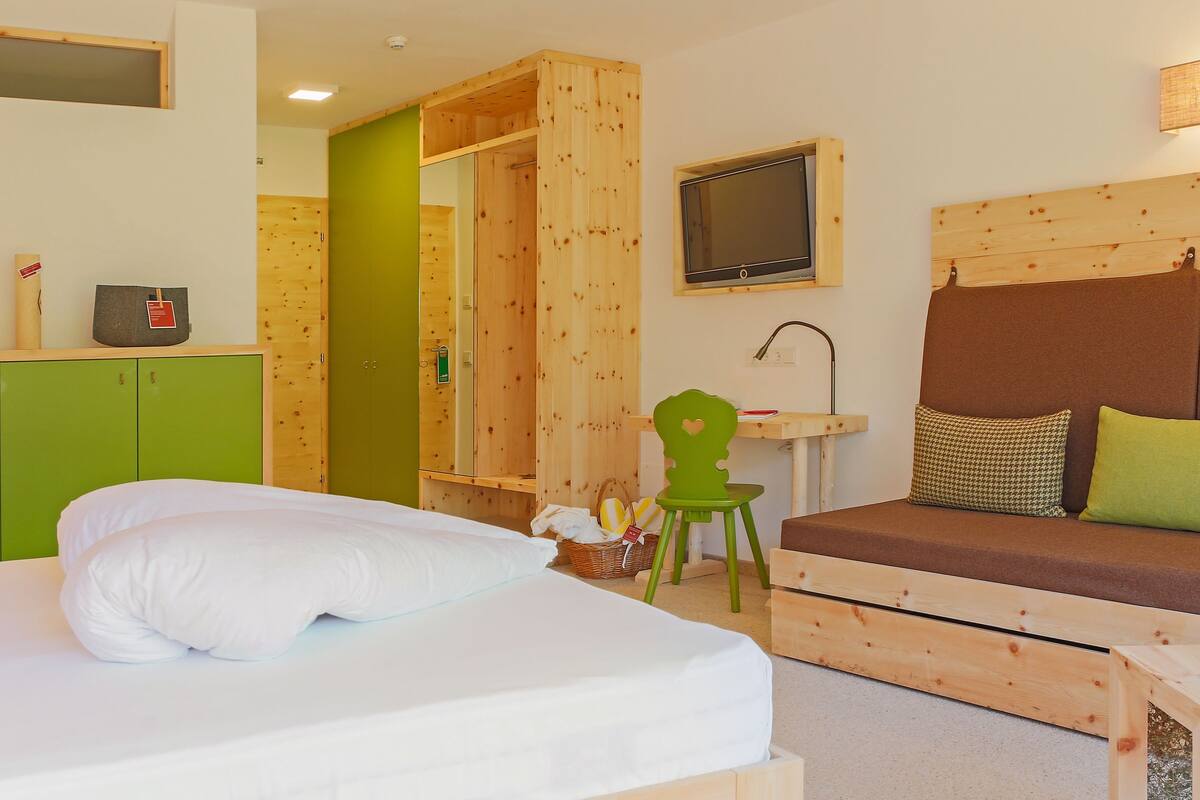 Ein Hotelzimmer mit Bett, einem grünen Kleiderschrank, einem Holz-Kopfstück, einem Fernseher und einem kleinen Tisch.