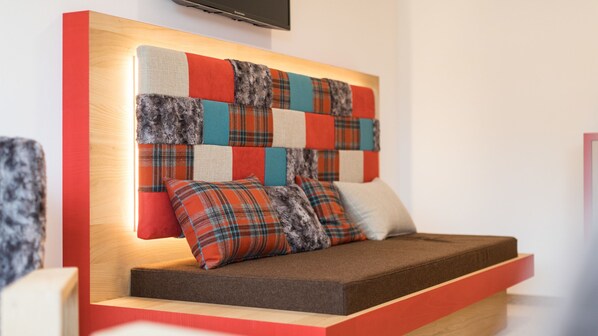 A modern room with a unique headboard design, a built-in bench, and a flat-screen TV mounted on the wall.