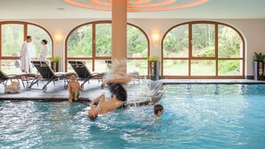 Una piscina interior con una fuente central, sillas de descanso y grandes ventanales que ofrecen vistas al exterior.