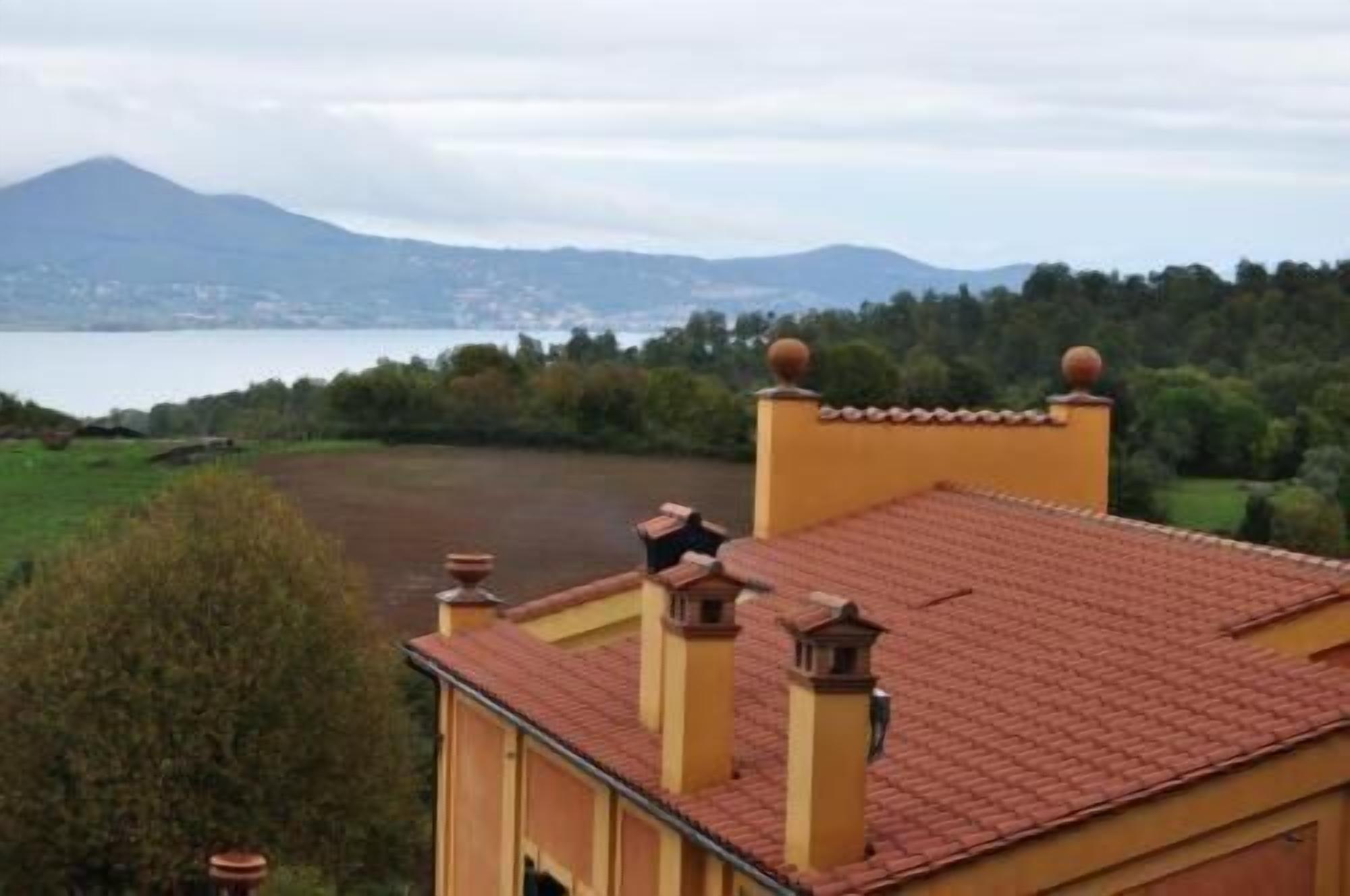 A building with a red-tiled roof, yellow walls, and a view of a lake and mountains in the background.