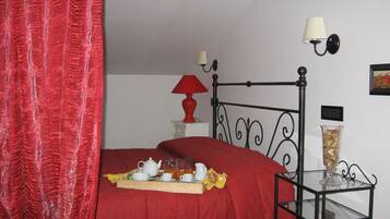 Un dormitorio con una colcha roja, una mesita de noche con una lámpara roja, una mesa de centro de cristal y una bandeja con objetos para té.