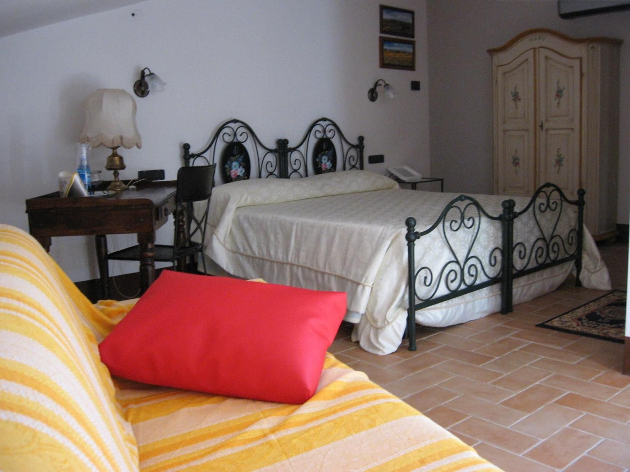 Une chambre à coucher avec un lit, une table de chevet, une lampe, une armoire et un coussin rouge sur un canapé à rayures.