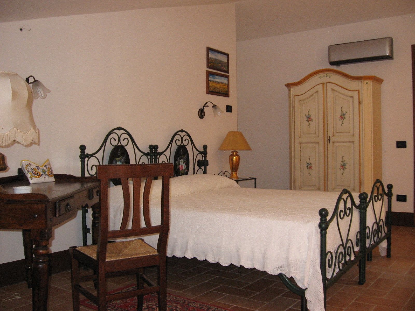 A bedroom with a bed, a chair, a desk, a lamp, and a wardrobe.