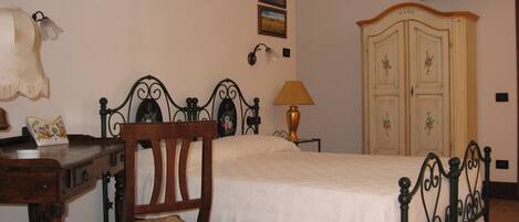 A bedroom with a bed, a chair, a desk, a lamp, and a wardrobe.