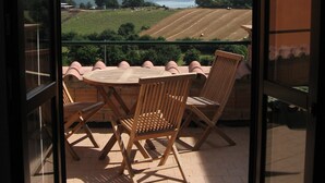 Un balcon agrémenté d’une table et de chaises, offrant une vue sur un paysage composé de champs et de montagnes lointaines.