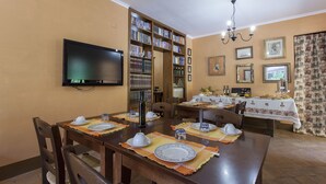 Un coin repas avec une longue table dressée pour quatre personnes, entouré d’étagères à livres et d’un téléviseur.