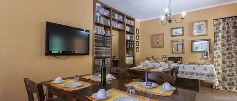 A dining area with a long table set for four, surrounded by bookshelves and a television.