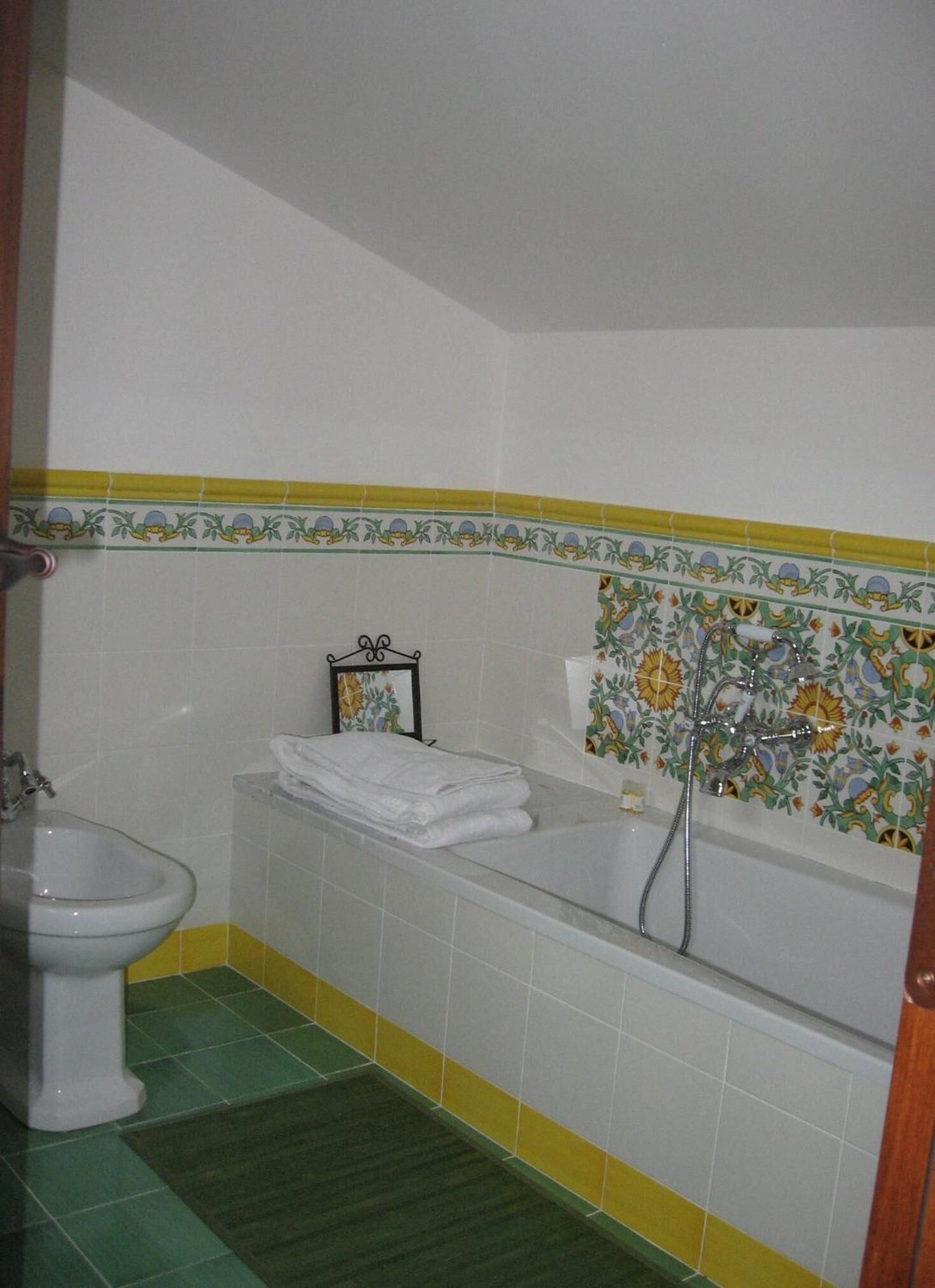 Baño con inodoro, lavabo y bañera. Se observa un perchero con toallas dobladas y un cuadro en la pared.