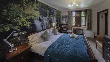 A bedroom with a large mural of a waterfall, a wooden bed with a blue quilt, a nightstand with a lamp, and a window with curtains.