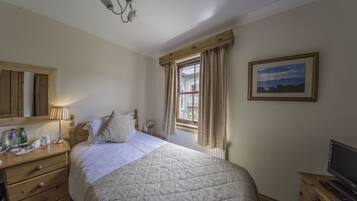 A neatly arranged bedroom with a bed, bedside table, lamp, and a painting on the wall.