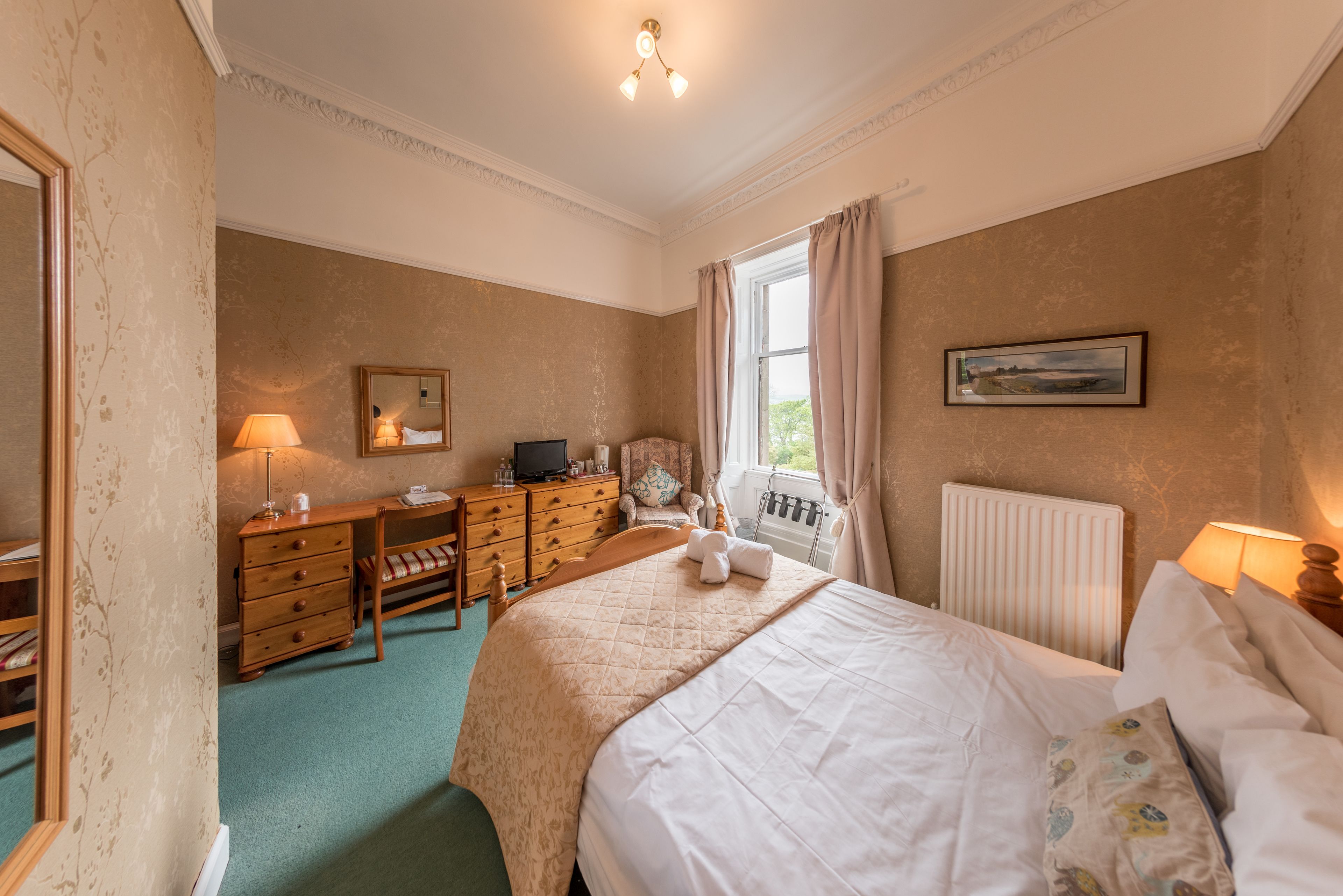 Une chambre à coucher comprenant un lit, une commode, un bureau, une chaise et une fenêtre avec des rideaux.
