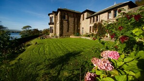 Un grand bâtiment en pierre, avec une pelouse bien entretenue et des plantes en fleurs au premier plan.